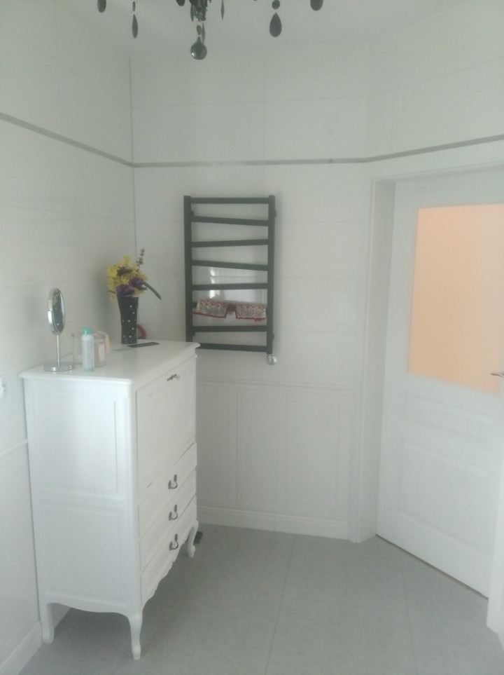 Biała łazienka z grzejnikiem drabinkowym, komodą z dekoracjami i oświetleniem sufitowym w stylu glamour.