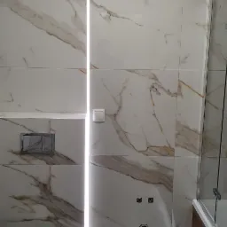 Wykończona łazienka z marmurowymi płytkami, podświetleniem LED w pionowej szczelinie i wiszącą toaletą.