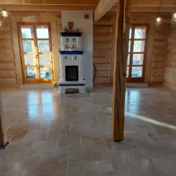 Wykończona podłoga z trawertynu w nowym domu z drewnianymi ścianami i ozdobnym piecem kaflowym.