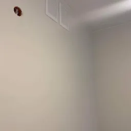 Świeżo pomalowana ściana w jasnym odcieniu z dwoma białymi kratkami wentylacyjnymi i otworem na kabel elektryczny bez wykończenia.