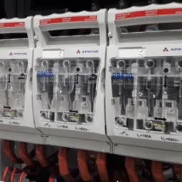 Trzy rozłączniki bezpiecznikowe APATOR RBK00 zamontowane w szafie elektrycznej, widoczne przewody zasilające w pomarańczowej izolacji.