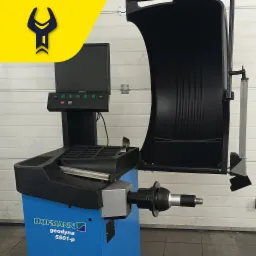 Wyważarka do kół Hofmann Geodyna 5501-p z czarną osłoną i panelem sterowania z zielonymi przyciskami, ustawiona w warsztacie na tle białej ściany z paneli.