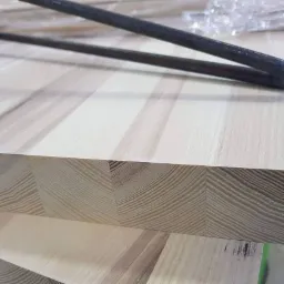 Krawędź blatu z klejonego drewna o jasnym odcieniu, widoczne słoje i struktura, na wierzchu metalowe rury.