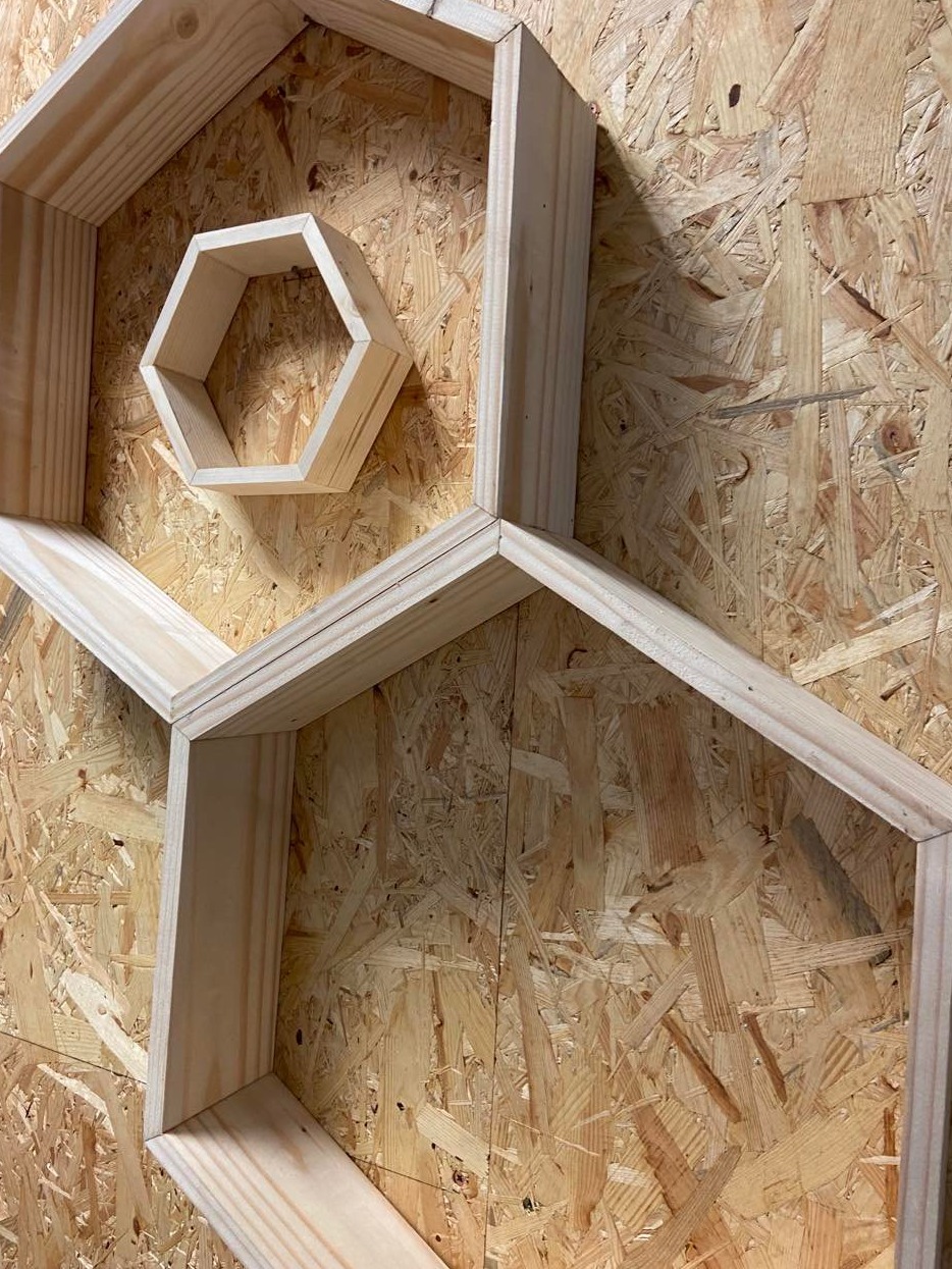 Drewniane, surowe półki w kształcie sześciokątów, zamontowane na płycie OSB, widoczne z bliska pod kątem.