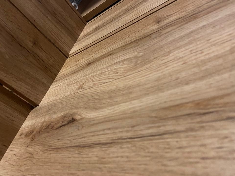 Szczegółowe ujęcie blatu z naturalnego drewna o wyraźnym usłojeniu, z widocznymi krawędziami i delikatnymi przebarwieniami, sfotografowane pod kątem.