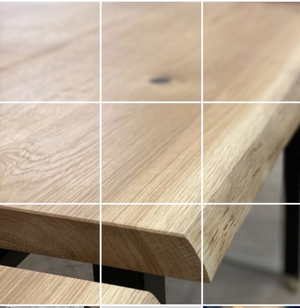 Zbliżenie na jasny, dębowy blat stołu z wyraźnym usłojeniem i subtelnym, naturalnym przebarwieniem, wsparty na czarnej, metalowej podstawie.