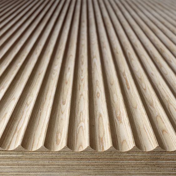 Faliste, profilowane panele z jasnego drewna z widocznym usłojeniem, ułożone równolegle, tworzące dekoracyjną powierzchnię.