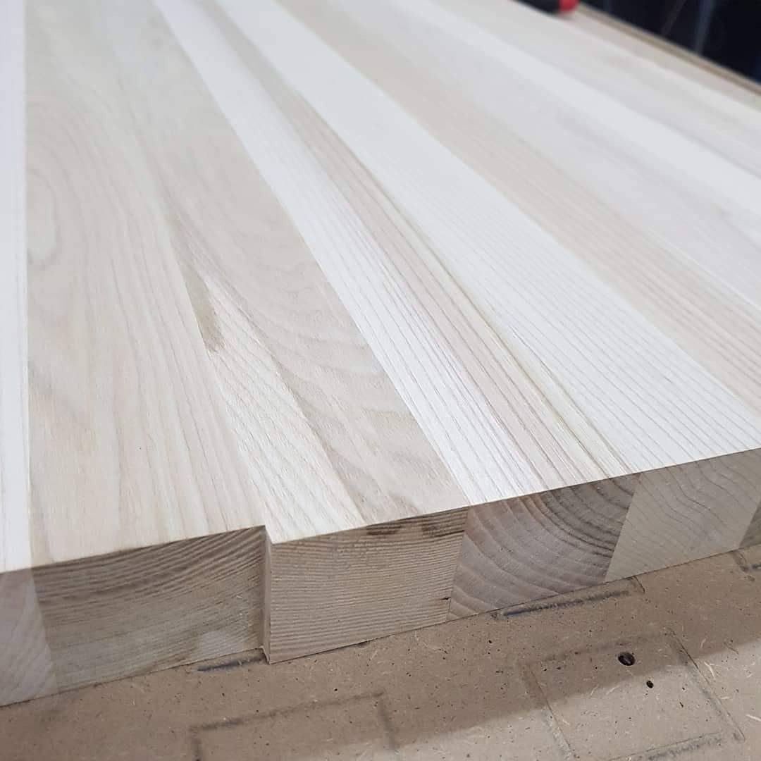 Jasny blat z drewna klejonego, widoczne łączenia desek na szerokość, z charakterystycznym wycięciem na krawędzi, surowe drewno przed wykończeniem.