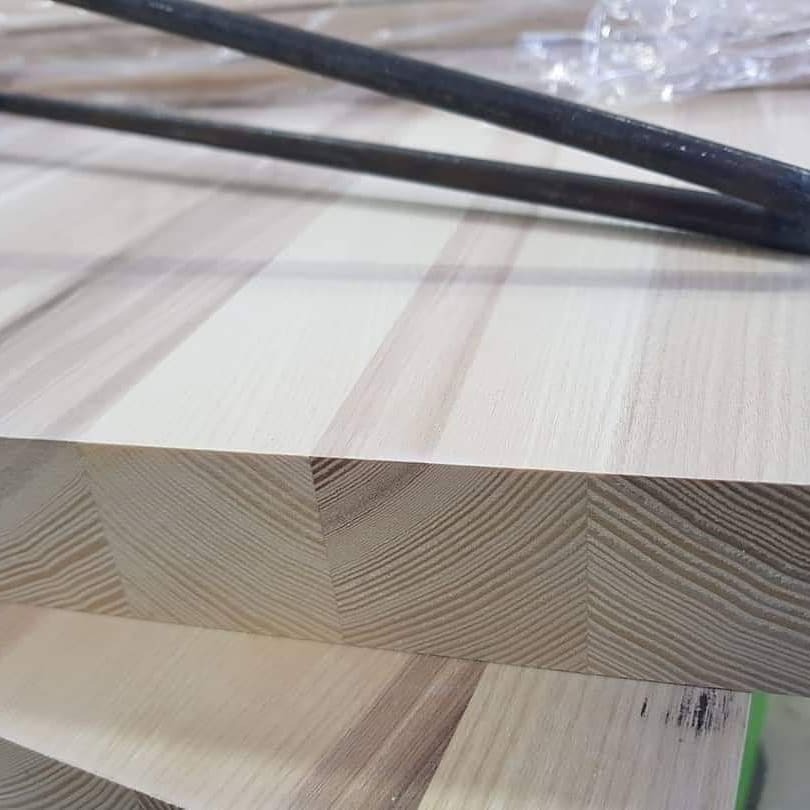 Krawędź blatu z klejonego drewna o jasnym odcieniu, widoczne słoje i struktura, na wierzchu metalowe rury.