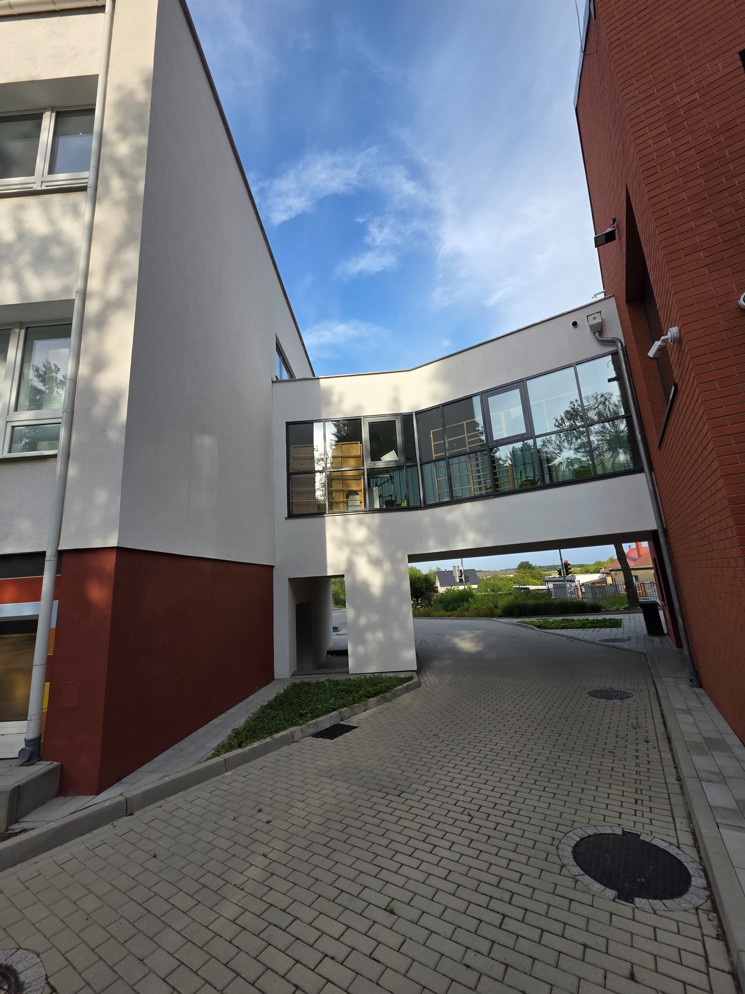 Nowoczesny budynek z łącznikiem między częściami, widok z dołu, ceglana elewacja i jasna fasada, kostka brukowa na podjeździe. Elementy architektury.