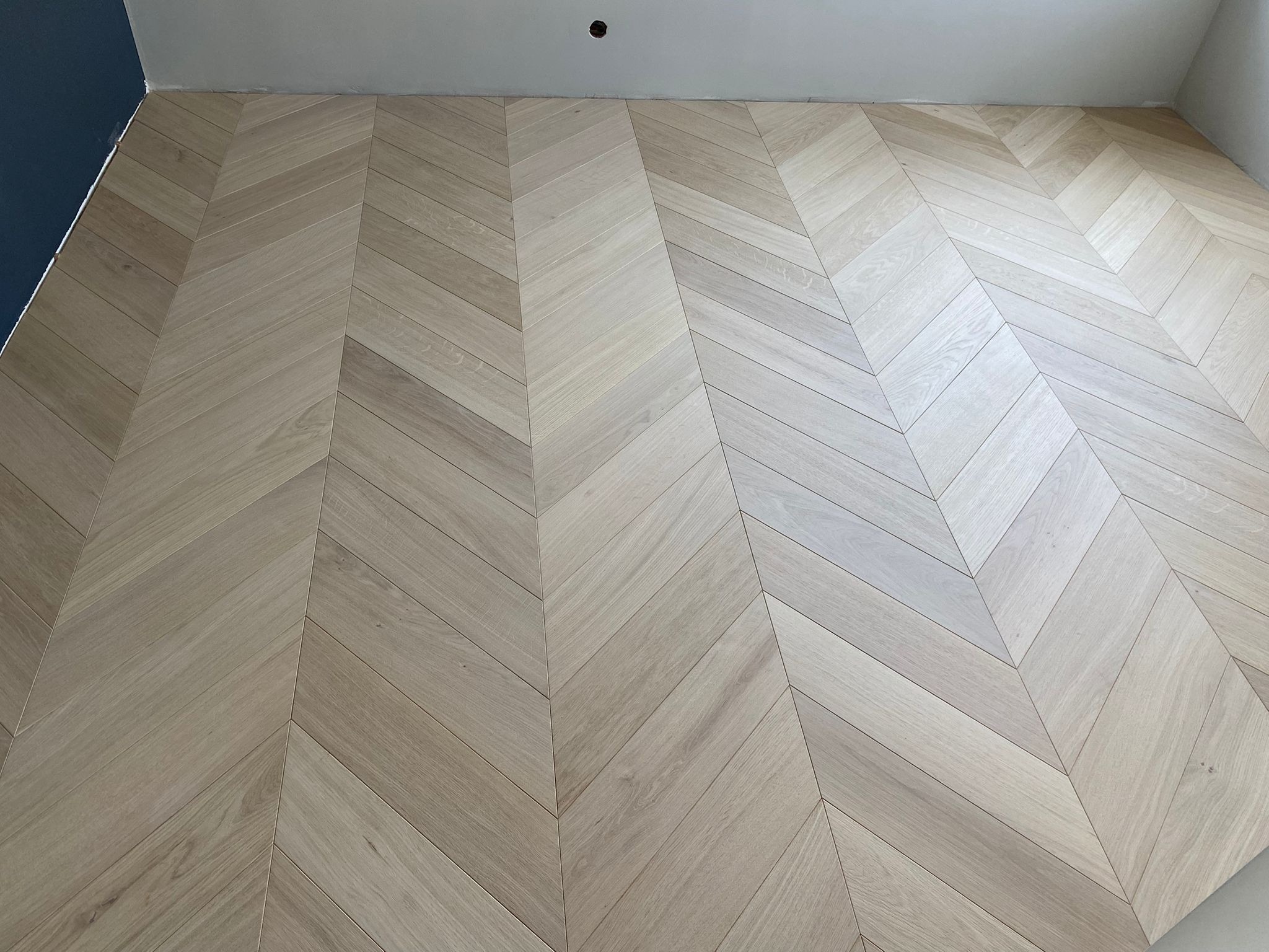 Jasny parkiet ułożony we wzór jodełki francuskiej, widok z góry. Minimalistyczne wnętrze z fragmentem niebieskiej ściany. Nowoczesne wykończenie podłogi.