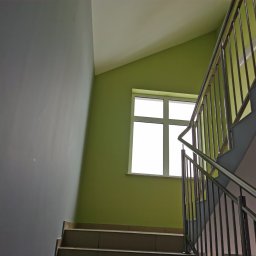 TP REMONTY I WYKOŃCZENIA - Klatka schodowa z metalową balustradą, ściany pomalowane na zielono i szaro, okno z białymi ramami w tle.