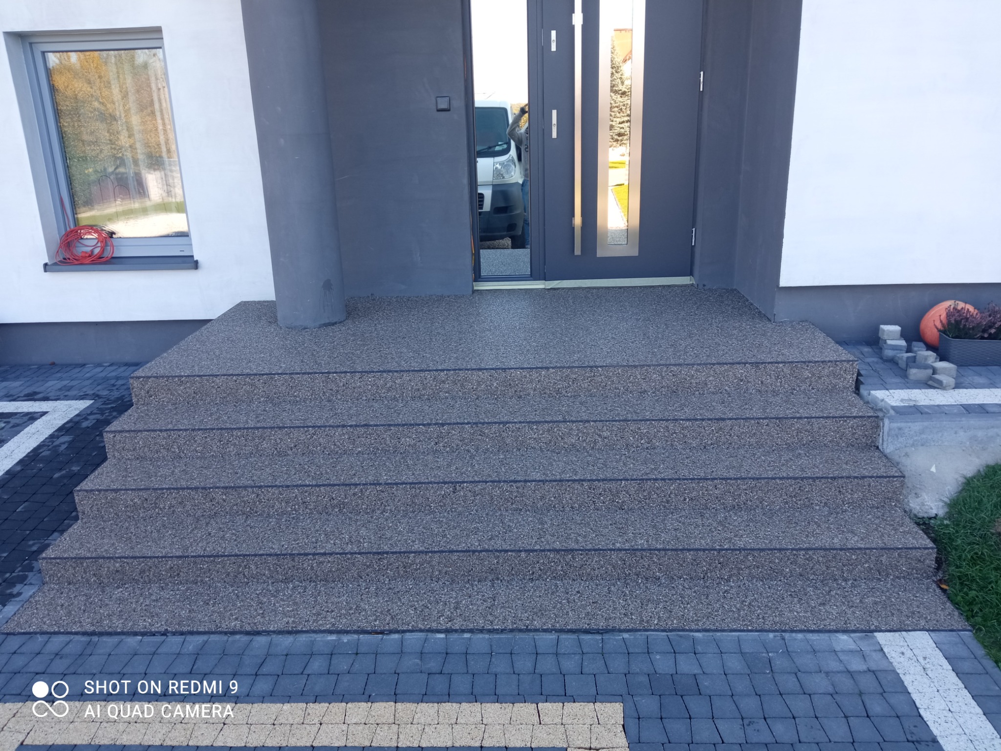 Schody wejściowe do domu wykończone posadzką żywiczną w kolorze szarym, dopasowane do elewacji i kostki brukowej.