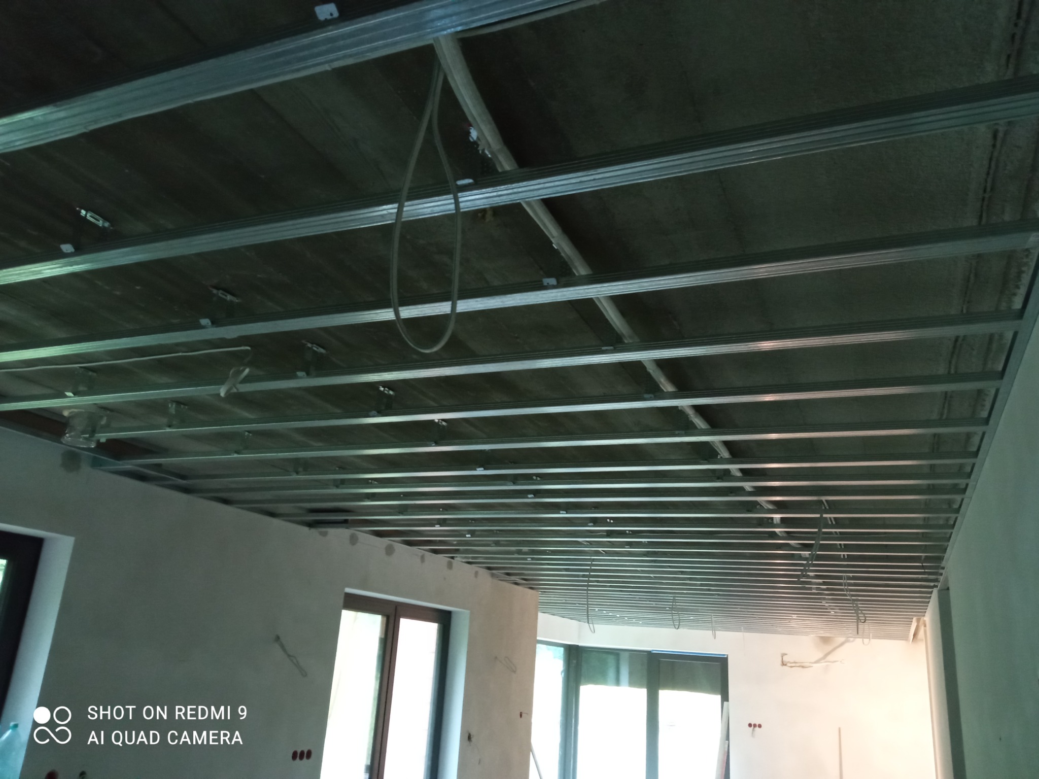 Metalowa konstrukcja sufitu podwieszanego, widoczne profile i mocowania, szary surowy strop w tle, w pomieszczeniu w trakcie prac wykończeniowych.