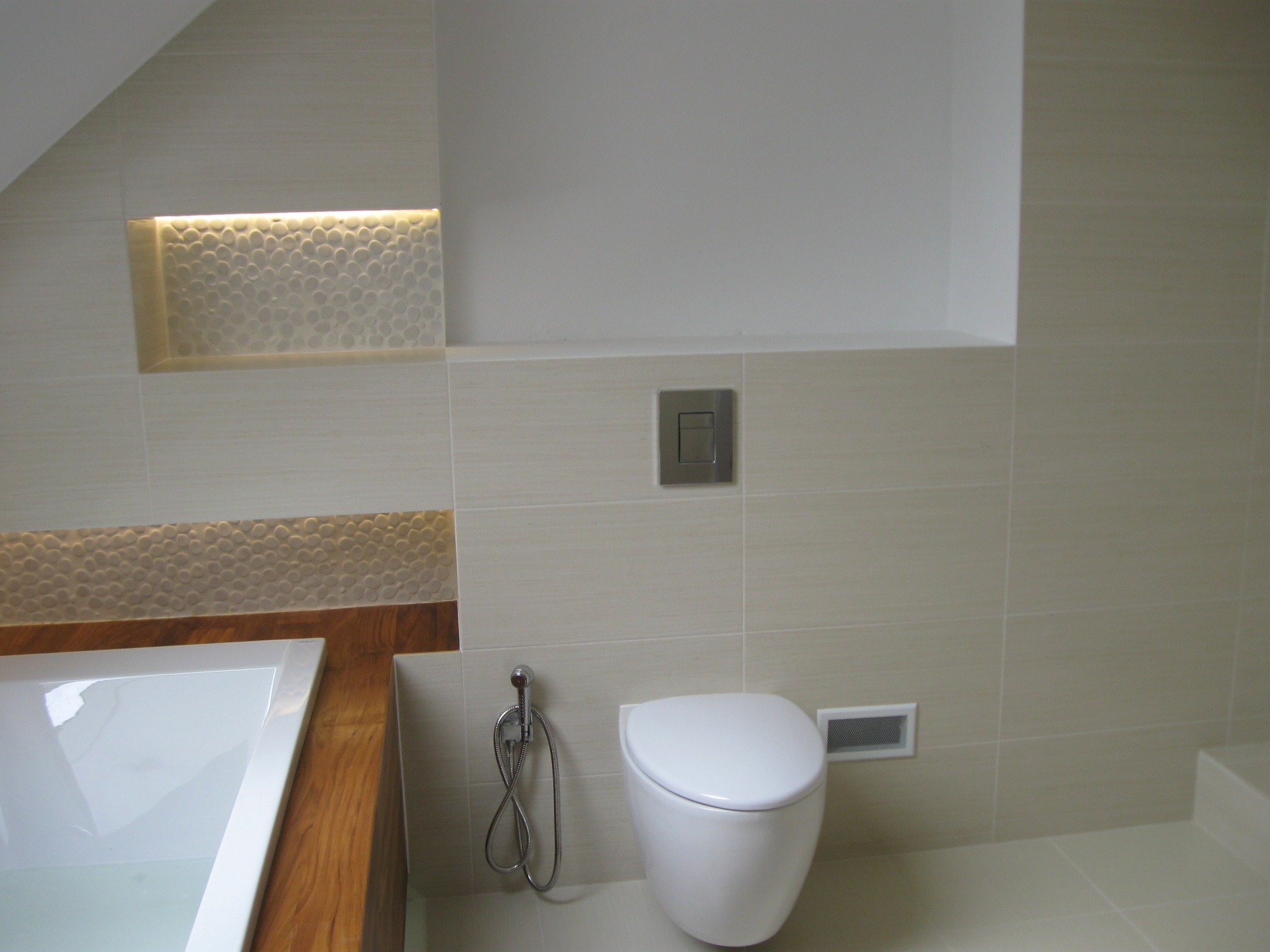 Nowoczesna łazienka w beżowych płytkach z podświetlaną wnęką nad wanną z drewnianą obudową i wiszącą toaletą z bidetką.