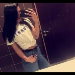 Osoba robi selfie w łazience z brązowymi płytkami i ciemnymi drzwiami.