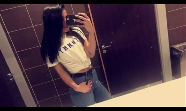 Osoba robi selfie w łazience z brązowymi płytkami i ciemnymi drzwiami.