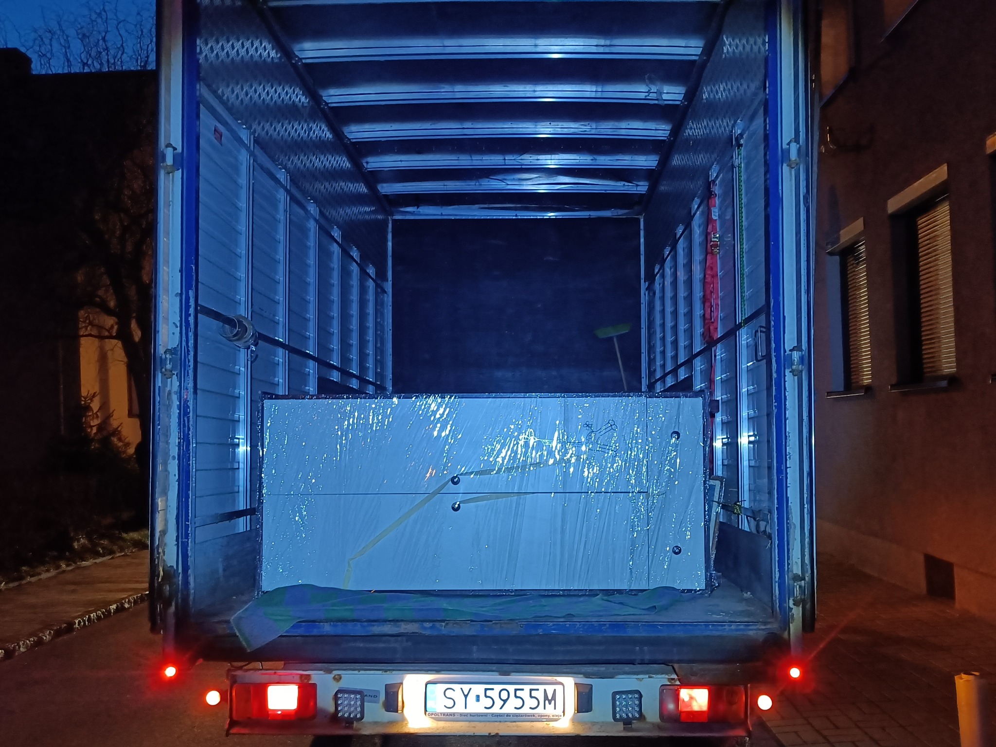 Wnętrze skrzyni ładunkowej samochodu dostawczego z zabezpieczonym ładunkiem, widok z tyłu, oświetlenie nocne.