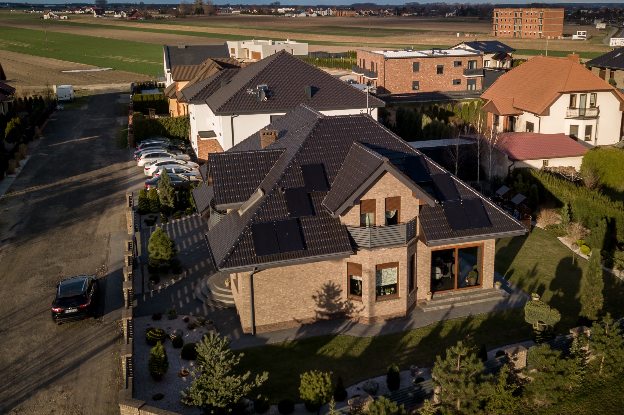 Widok z lotu ptaka na dom jednorodzinny z panelami słonecznymi na dachu, zaparkowanym samochodem i zadbanym ogrodem.