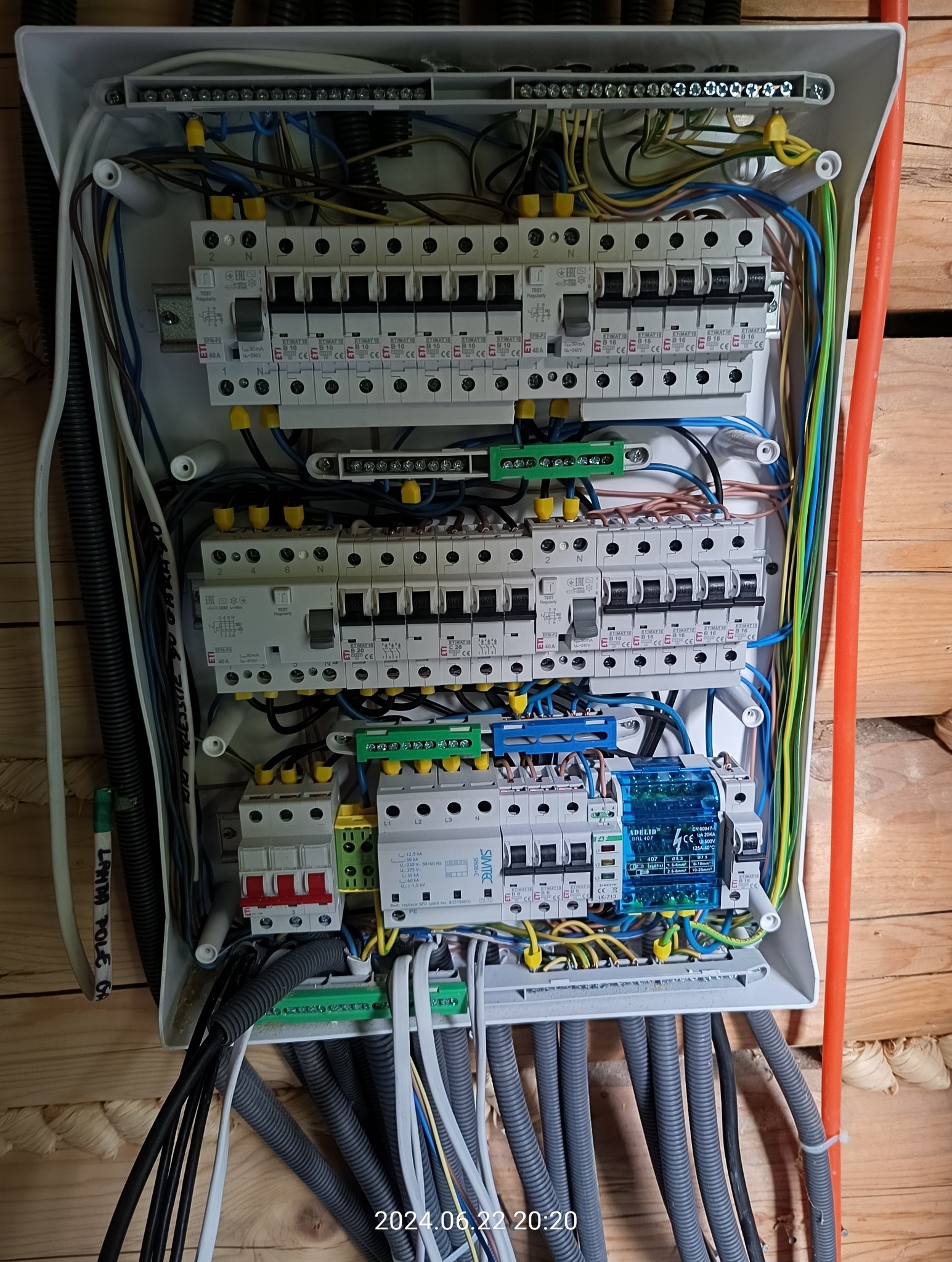 Rozdzielnica elektryczna z licznymi bezpiecznikami i przewodami, zamontowana na drewnianej ścianie, widok z bliska ukazujący szczegóły połączeń i komponentów.