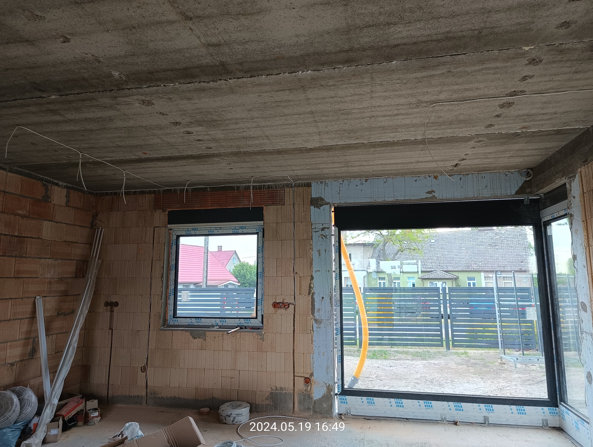 Surowy stan wnętrza w trakcie remontu: ściany z cegły dziurawki, betonowy sufit z prowizorycznie poprowadzonymi przewodami elektrycznymi, okna z PCV, widoczne puszki elektryczne, brak tynków.