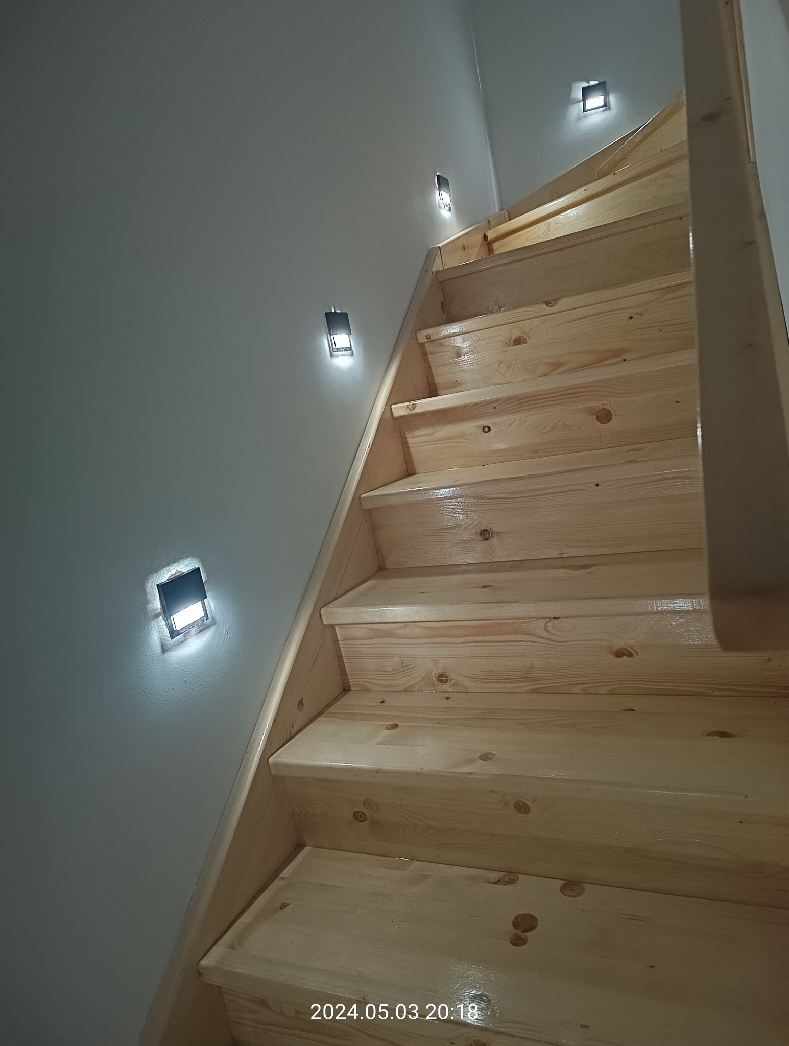 Drewniane schody z zamontowanym oświetleniem punktowym w ścianie, widok z dołu, świeżo po lakierowaniu.