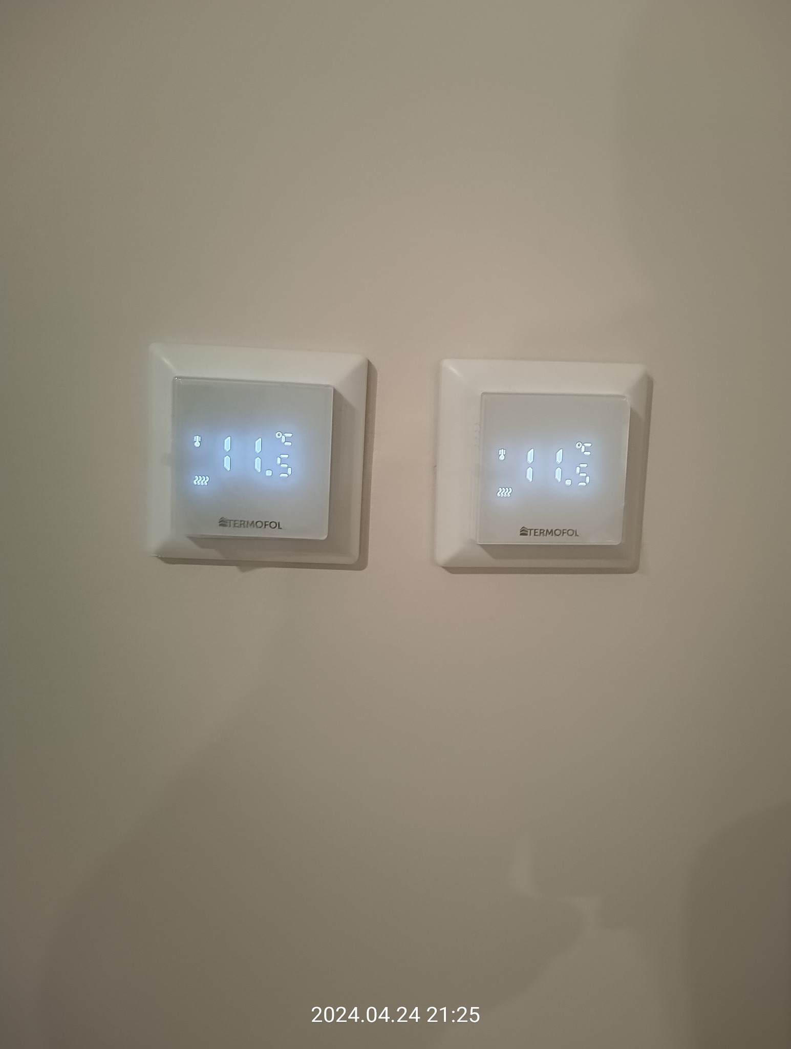 Dwa białe, kwadratowe termostaty firmy Termofol zamontowane na beżowej ścianie, wyświetlające temperaturę 10.5 stopni Celsjusza.