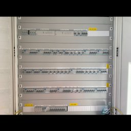 ElectroLine Marcin Zblewski - Rozdzielnica elektryczna z wieloma zabezpieczeniami różnicowoprądowymi i nadprądowymi, opisana etykietami, zamontowana wewnątrz białej szafki.