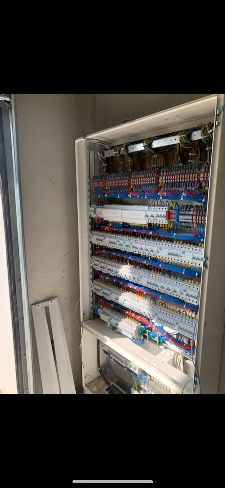 Otwarta skrzynka rozdzielcza z licznymi przewodami i bezpiecznikami, widoczne szyny montażowe i elementy zabezpieczające, obok ściana budynku.