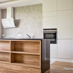 Kuchnia z wyspą otwarta na salon. W zabudowie kuchni białe lakierowane fronty z podchwytem i blat z konglomeratu.