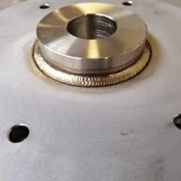 Precyzyjny spaw łączący okrągły element z metalową płytą, widoczne regularne spoiny i otwory montażowe w płycie.