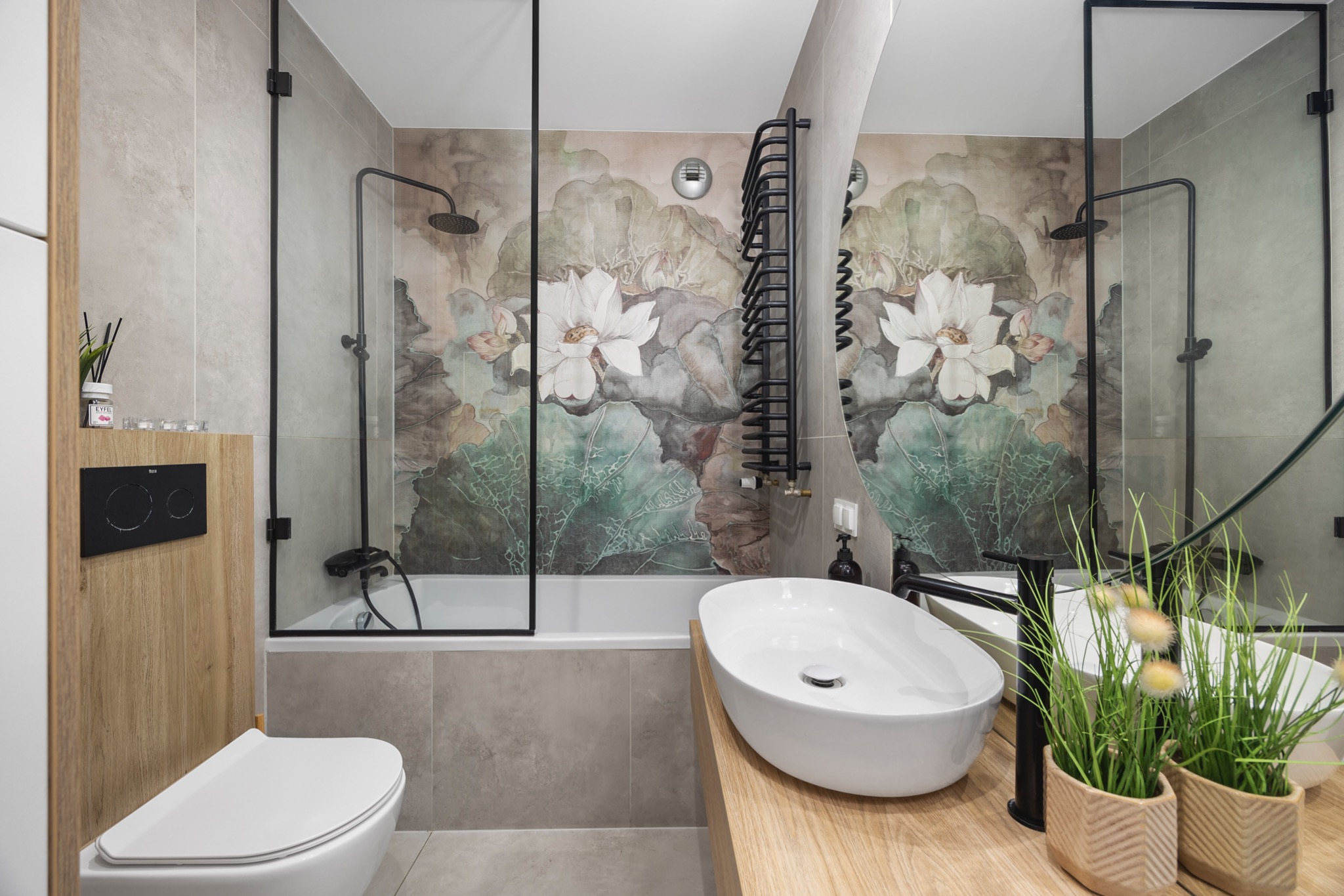 Nowoczesna łazienka z wanną za szklaną ścianką, umywalką nablatową na drewnianym blacie i tapetą w kwiaty lotosu, oświetlona ciepłym światłem.