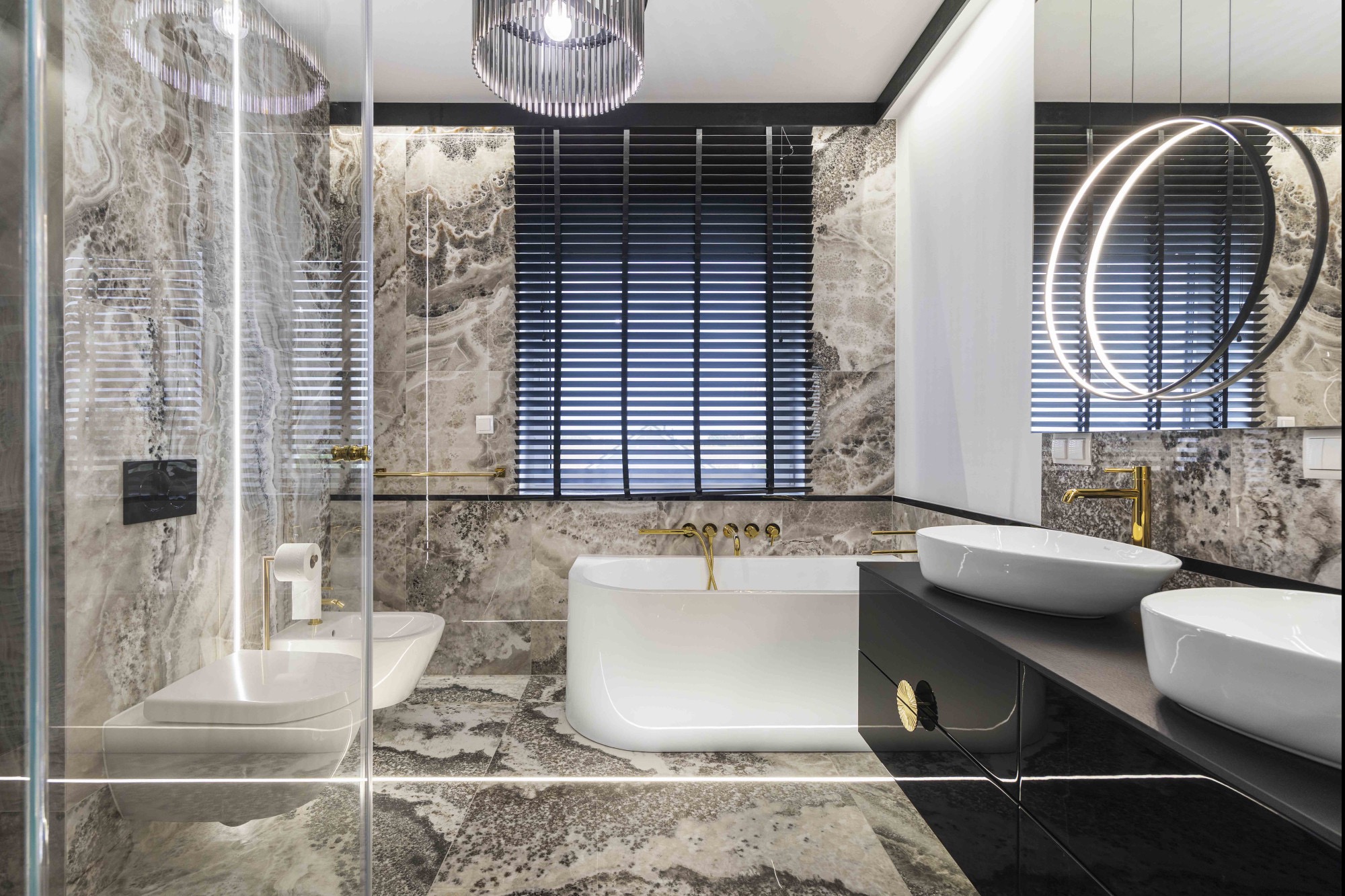 Elegancka łazienka z marmurowymi płytkami, białą wanną i umywalkami nablatowymi. Złote akcenty armatury i oświetlenia. Nowoczesny design z żaluzjami w oknie.
