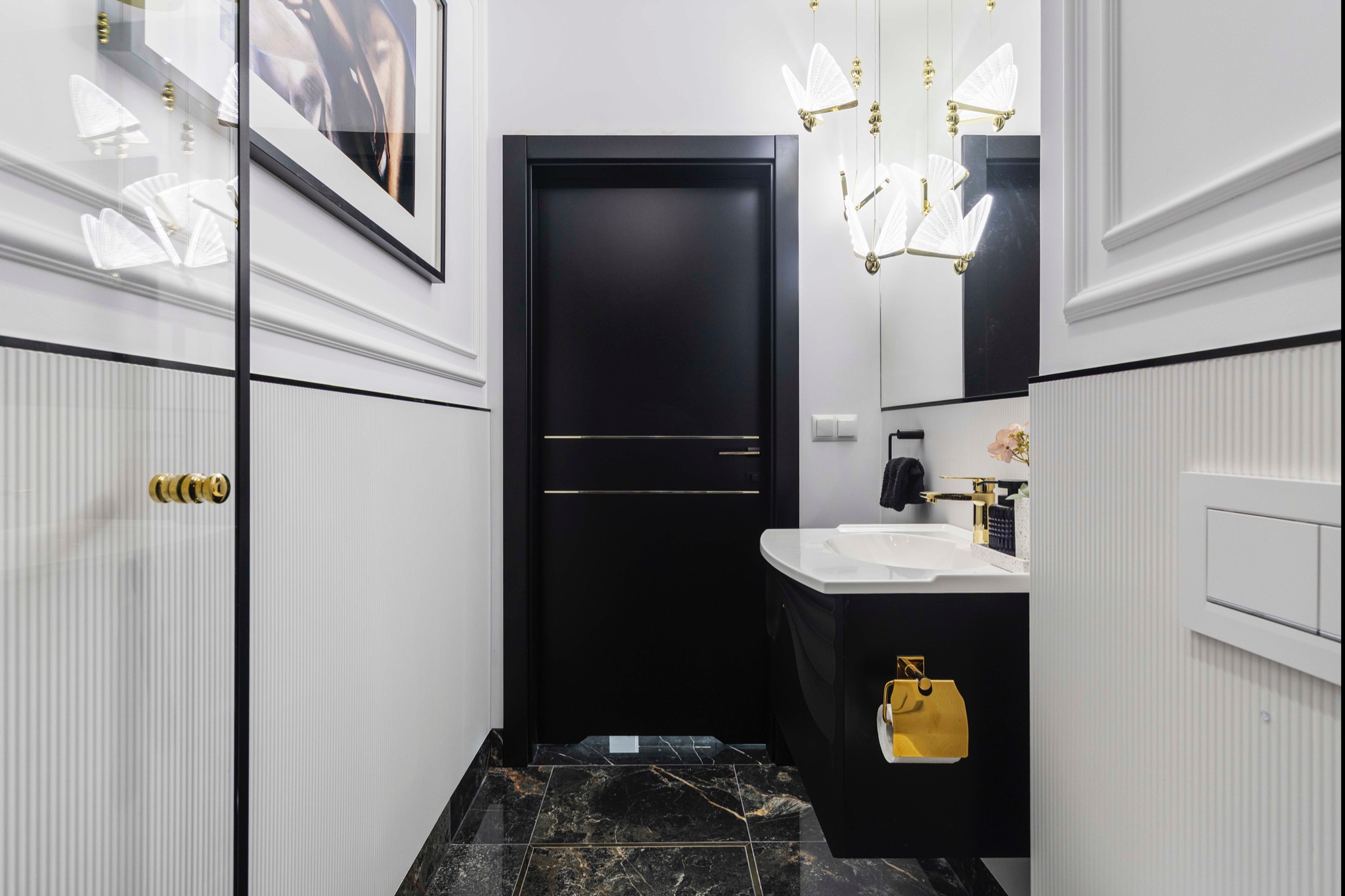 Elegancka łazienka w czerni i bieli z marmurową podłogą, złotymi akcentami i designerskim oświetleniem motylkowym. Nowoczesny wystrój wnętrza.