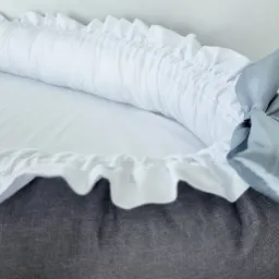 Dziecięcy kokon niemowlęcy z szarego lnu i białej satyny, wykończony falbanką i ozdobną, błękitną wstążką.