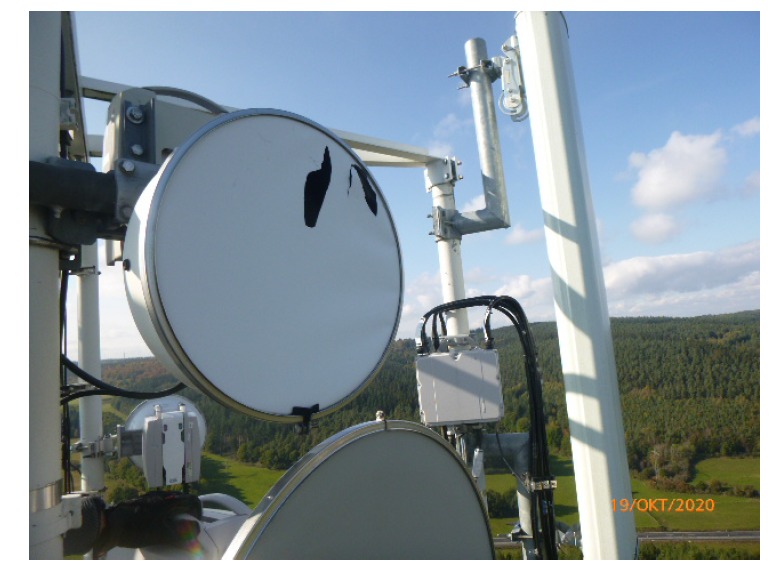 Anteny telekomunikacyjne na wieży z widocznymi uszkodzeniami na jednej z anten parabolicznych i datą 19/OKT/2020 w prawym dolnym rogu.