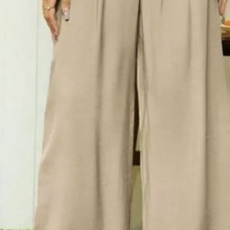 1LS Iryna Kozarenko - Beżowe, szerokie spodnie damskie z zakładkami, prezentowane na modelce z zielonymi sandałami na sztucznej trawie.