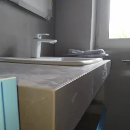 Nowoczesna umywalka z szarą, marmurkową konsolą w trakcie montażu, widoczne narzędzia i okno w tle.