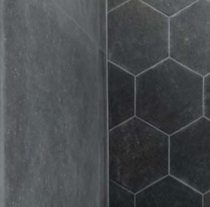 Szara ściana z efektem betonu sąsiaduje z fragmentem ściany wyłożonej heksagonalnymi, ciemnymi płytkami z jasną fugą.