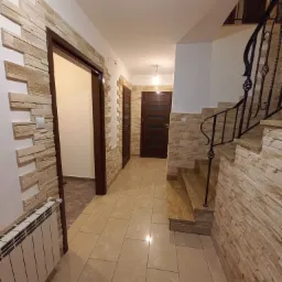 Korytarz wykończony panelami imitującymi kamień, z widocznymi schodami z metalową balustradą i grzejnikiem żeliwnym.