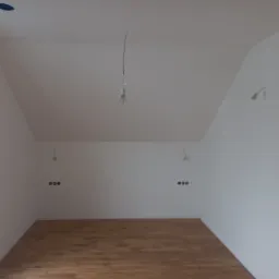 Poddasze po remoncie z drewnianą podłogą, świeżo pomalowanymi białymi ścianami i sufitem, widoczne niedokończone instalacje elektryczne, surowa żarówka zwisająca z sufitu.