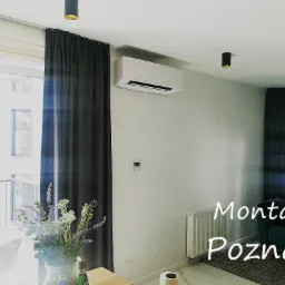 Nowoczesne wnętrze mieszkania z zamontowaną klimatyzacją ścienną, widok na balkon z kwiatami w wazonie.