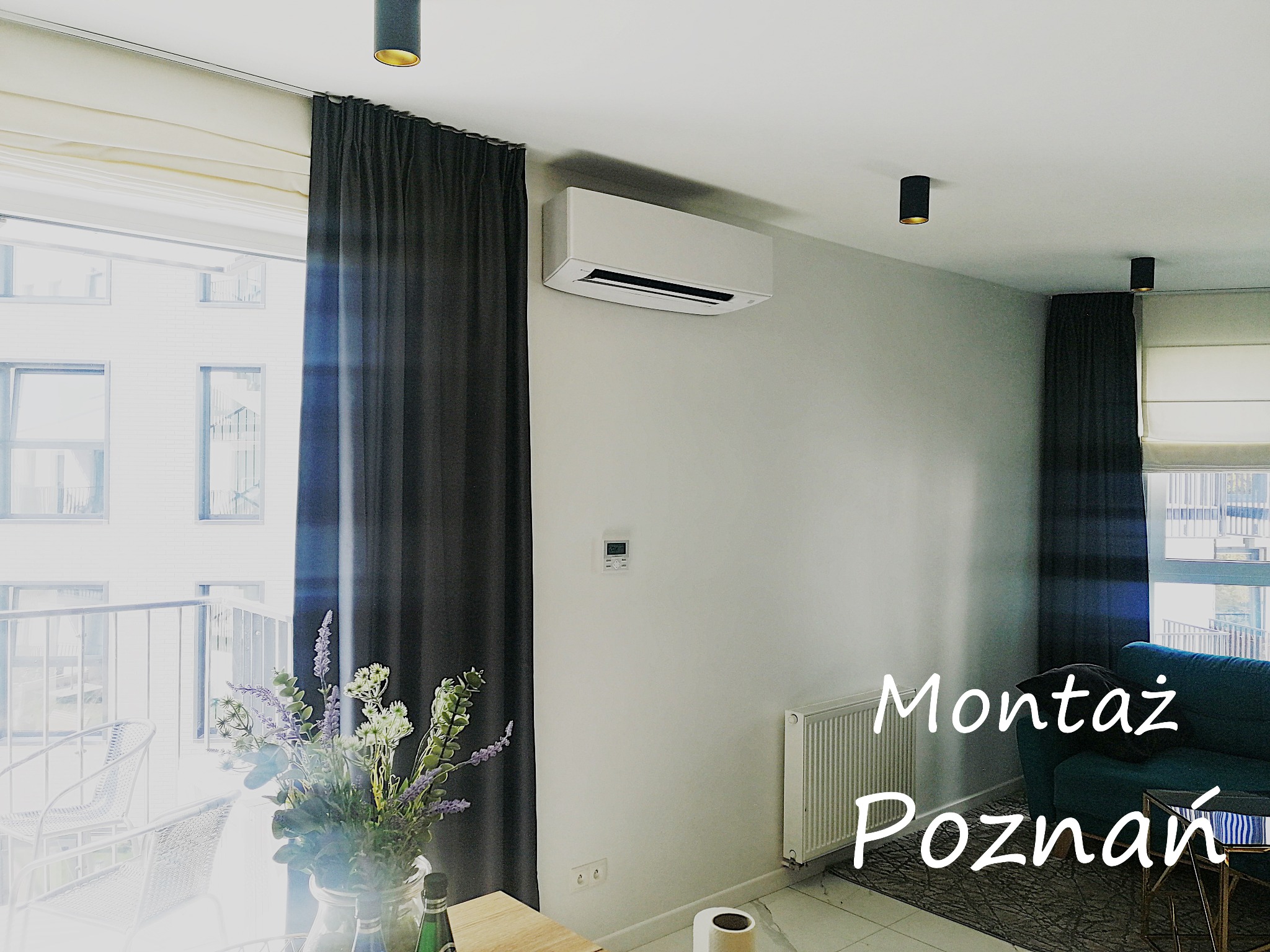 Nowoczesne wnętrze mieszkania z zamontowaną klimatyzacją ścienną, widok na balkon z kwiatami w wazonie.