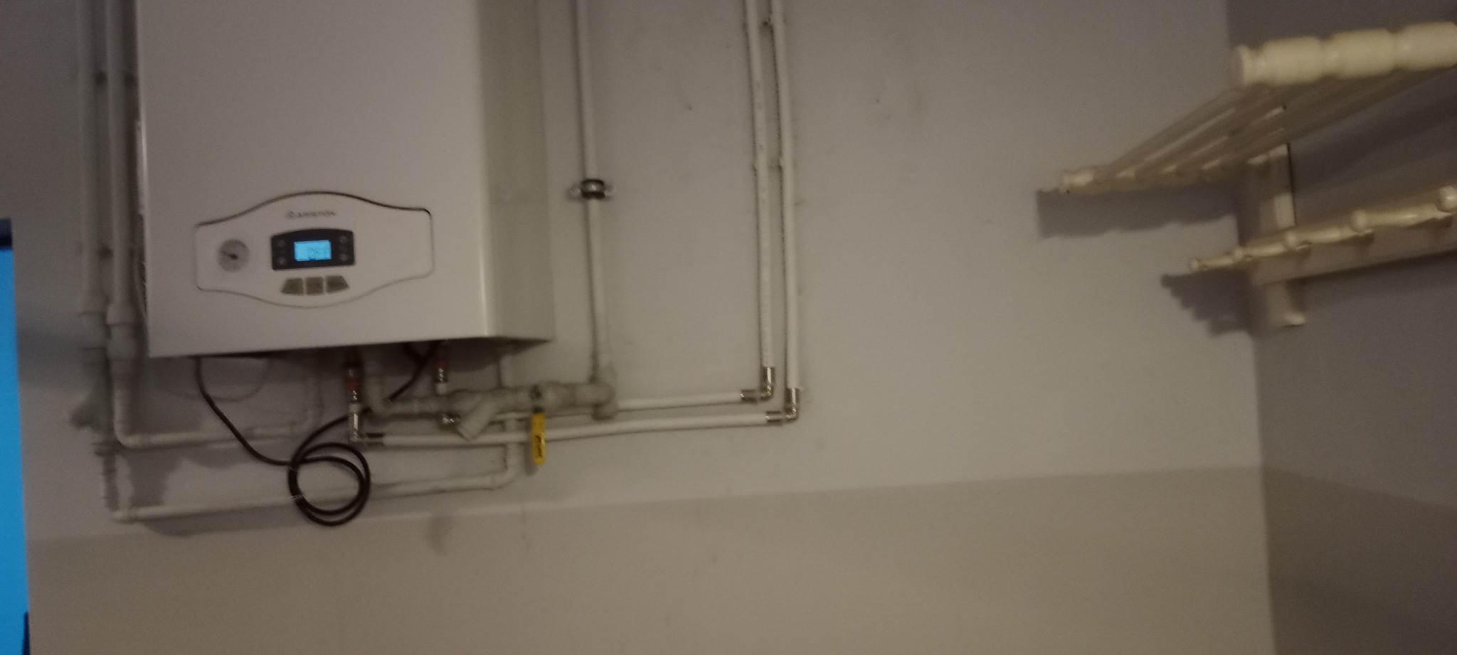 Kocioł gazowy Ariston zamontowany na ścianie z widocznymi rurami i przyłączami, obok wieszak na ręczniki.