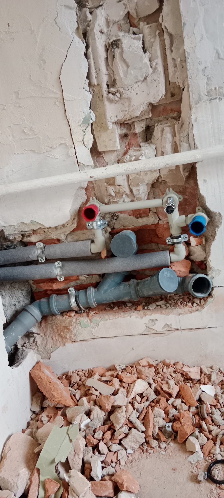 Odsłonięte rury wodne i kanalizacyjne w ścianie z widocznym fragmentem cegieł i gruzu po kuciu.