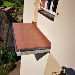 Wykończony balkon z terakotową okładziną, widok z góry, widoczne detale obróbki blacharskiej i elewacja budynku w odcieniach beżu.