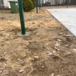 Artur Bąbiak - Przygotowanie terenu pod ogrodzenie z betonową wylewką, widoczne słupki w kolorze butelkowej zieleni, rozciągnięty sznurek wyznaczający linię, ziemia z liśćmi i śladami opon.