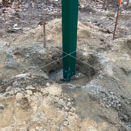 Artur Bąbiak - Zielony słupek ogrodzeniowy tymczasowo ustabilizowany w wykopanym otworze z pomocą sznurków i kołków, ziemia wokół wykopu.