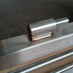 Detal spawania elementu metalowego: rura przyspawana do profilu, widoczne ślady spawania i przebarwienia.