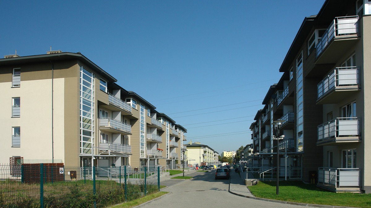 Nowoczesne budynki wielorodzinne z balkonami, elewacja w odcieniach beżu i brązu, widok z perspektywy ulicy w słoneczny dzień.